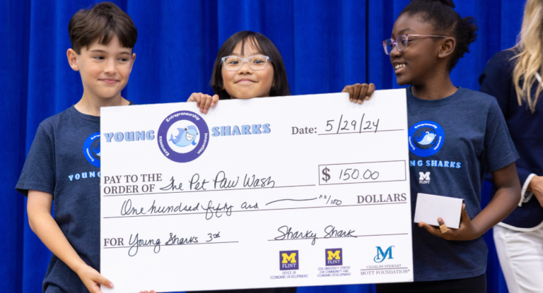 Three young K-12 students holding a giant check they won during the Young Sharks competition