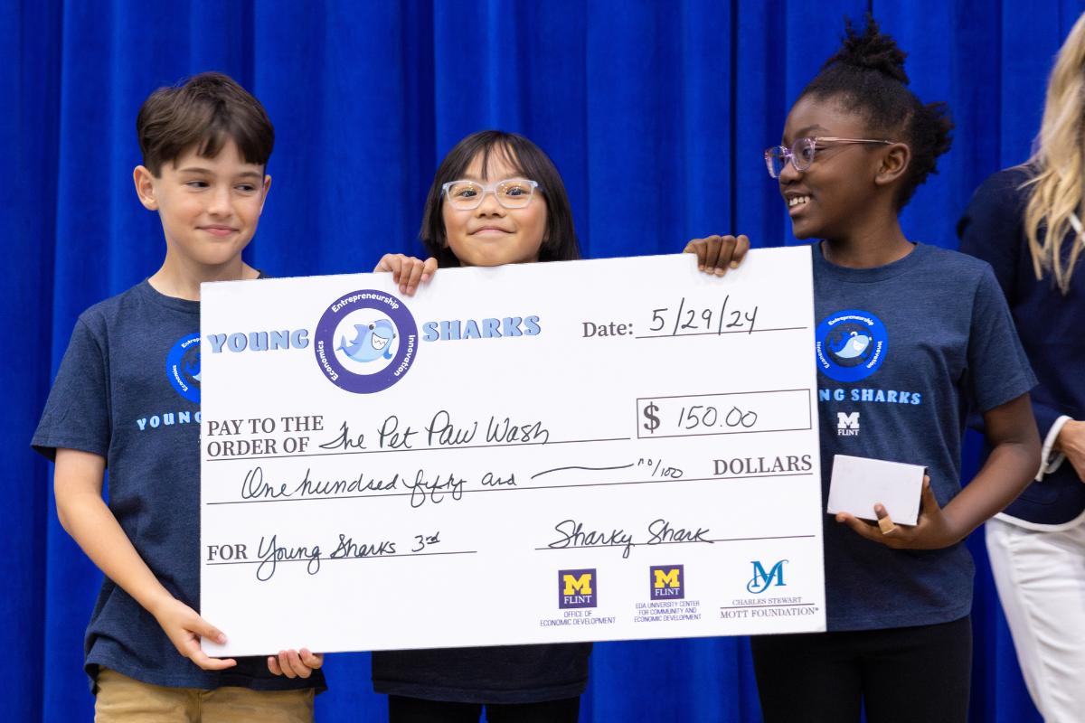 Three young K-12 students holding a giant check they won during the Young Sharks competition