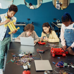 A diverse group of students building a robot with a teacher present.