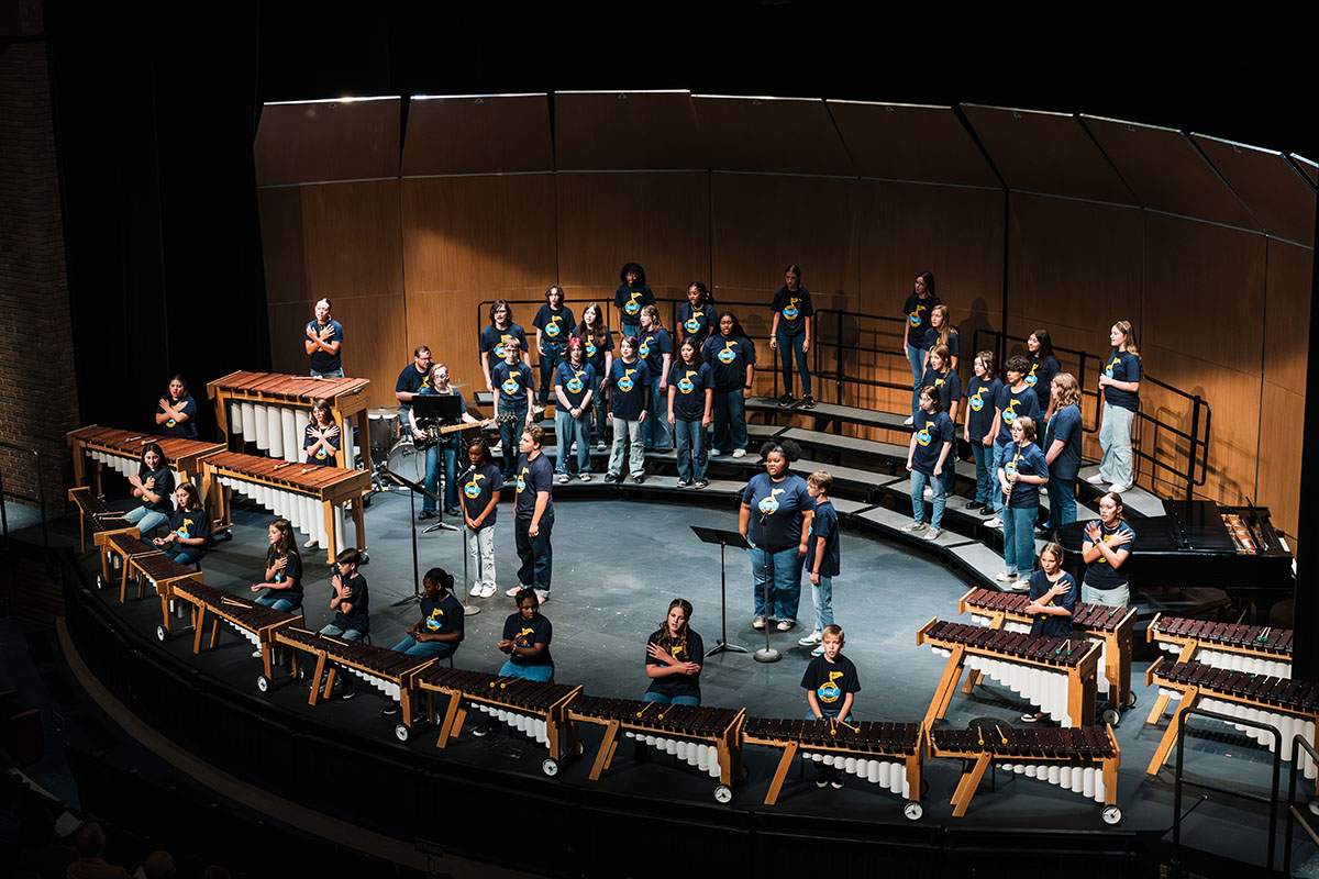 A wide shot of vocalists performing on risers on the stage with the audience seats visible in the foreground.