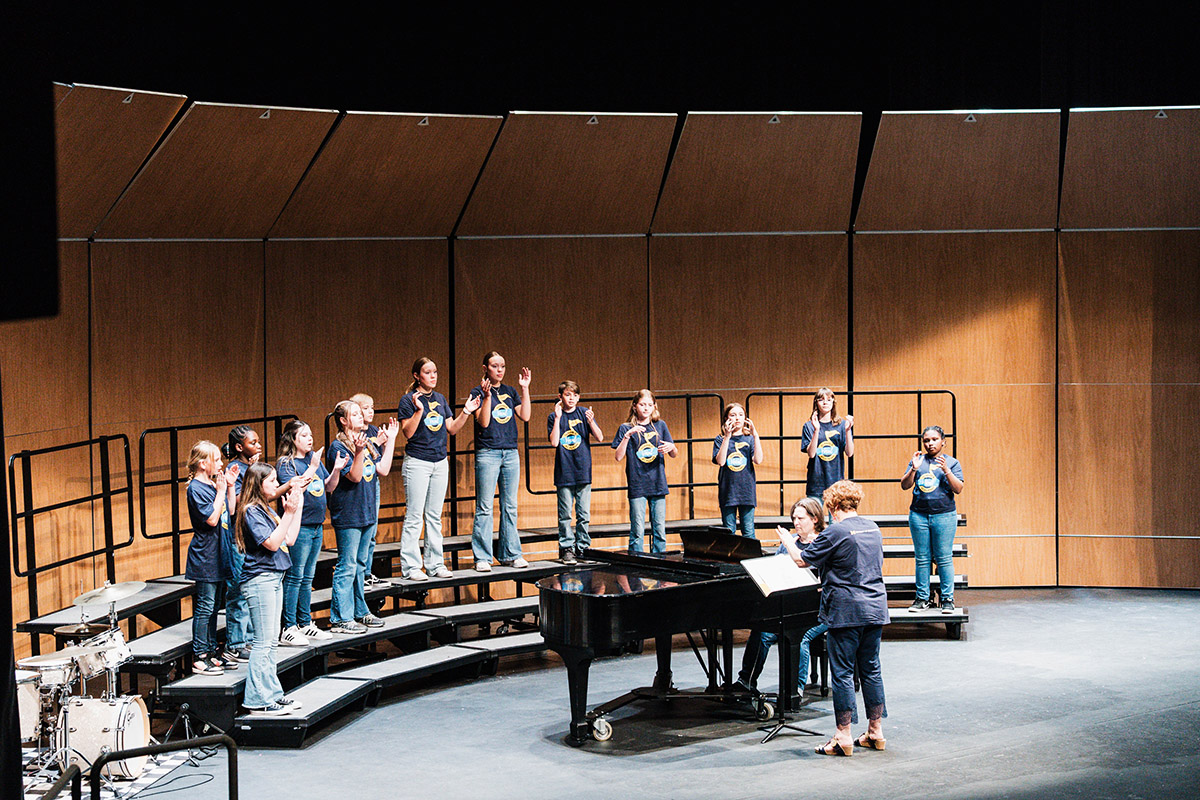 A wide shot of vocalists singing on risers on stage