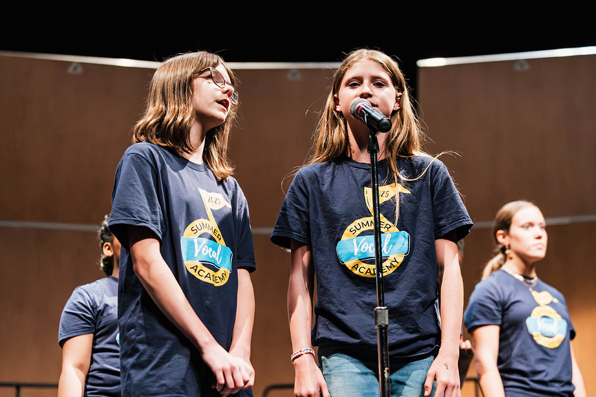 Two students singing into one microphone during the Summer Vocal Academy of Music.