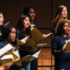A group of vocalists singing from sheet music during the Summer Vocal Academy of Music.