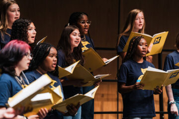 A group of vocalists singing from sheet music during the Summer Vocal Academy of Music.