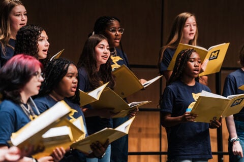 A group of vocalists singing from sheet music during the Summer Vocal Academy of Music.