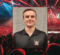 A headshot of Tomczyk in a WWE polo overlaid with a wrestling ring, crowd, and neon lights.