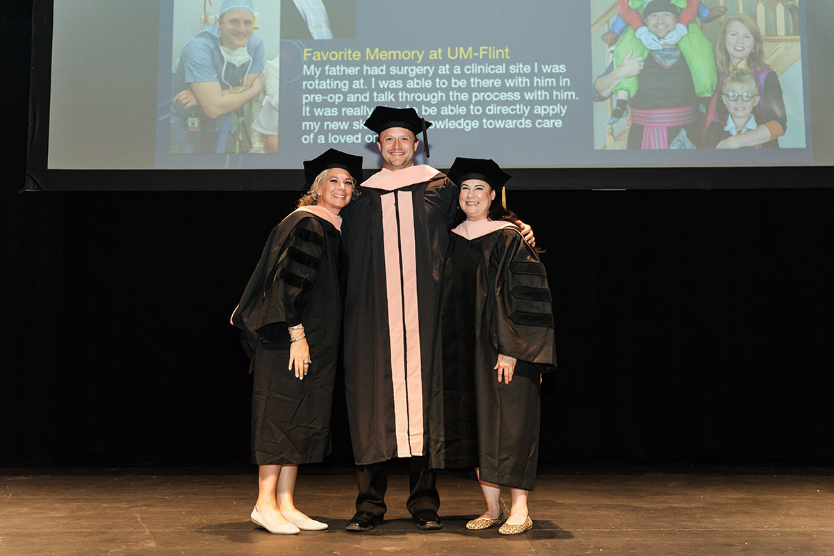 A female DNAP graduate posing for a photo on stage with faculty