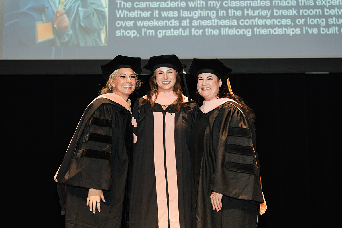 A female DNAP graduate posing for a photo on stage with faculty