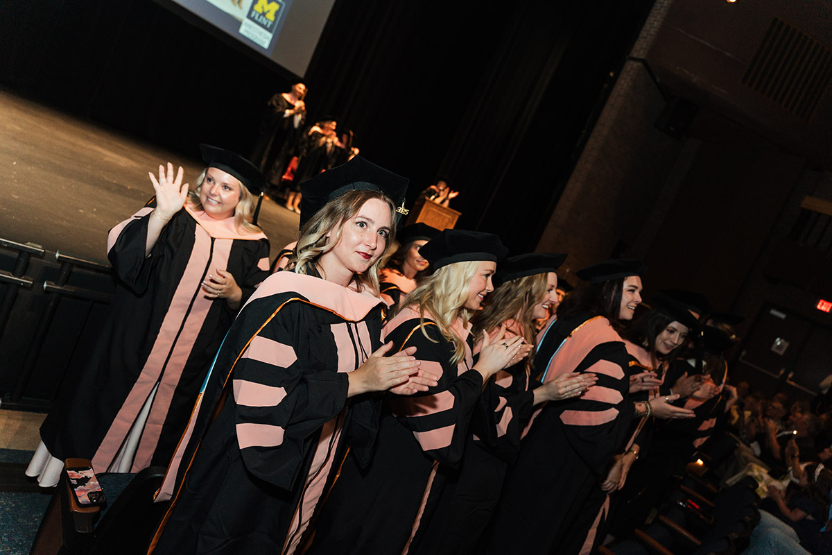 A group of DNAP graduates turning to face the crowd in the UM-Flint Theatre