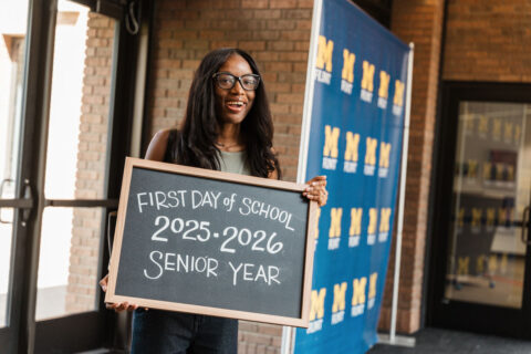 Smiling student holds a chalkboard sign marking the first day of senior year, 2025–2026.