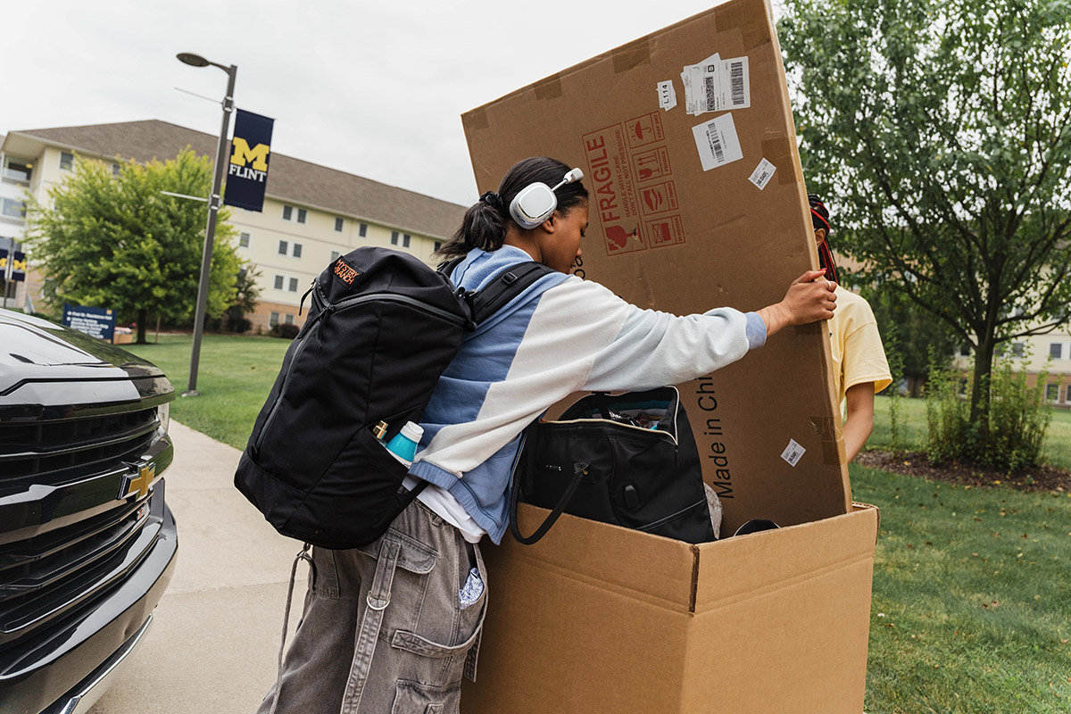 A UM-Flint student putting a large cardboard box inside of another box.