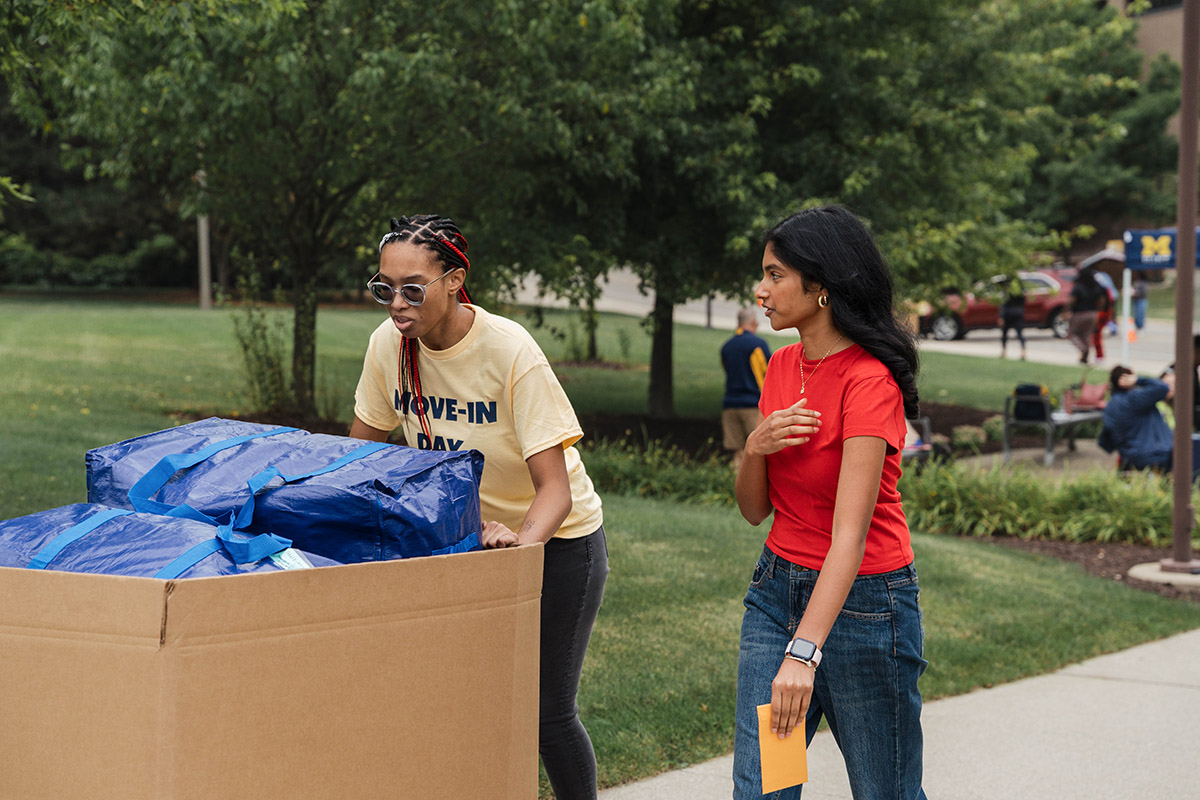 A UM-Flint student volunteer helping another student push her belongings inside.
