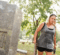 Melanie Purkis walking by a gravestone at Glenwood Cemetery wearing a gray tank top and black shorts