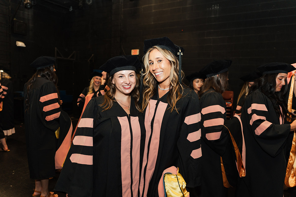 Two female DNAP graduates posing for a photo in their graduation regalia
