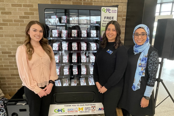Three UM-Flint students standing in front of a NARCAN vending machine.