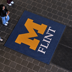 An overhead view of the first floor of the University Center with students walking close to a UM-Flint stamp logo on the floor.