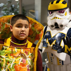 A young boy in a taco costume posing with the Wolverines Trooper, a star wars storm trooper with Michigan designs.