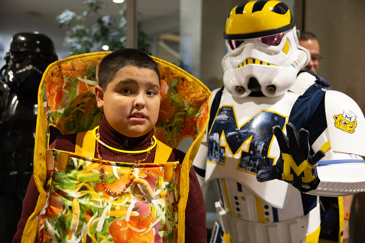 A young boy in a taco costume posing with the Wolverines Trooper, a star wars storm trooper with Michigan designs.