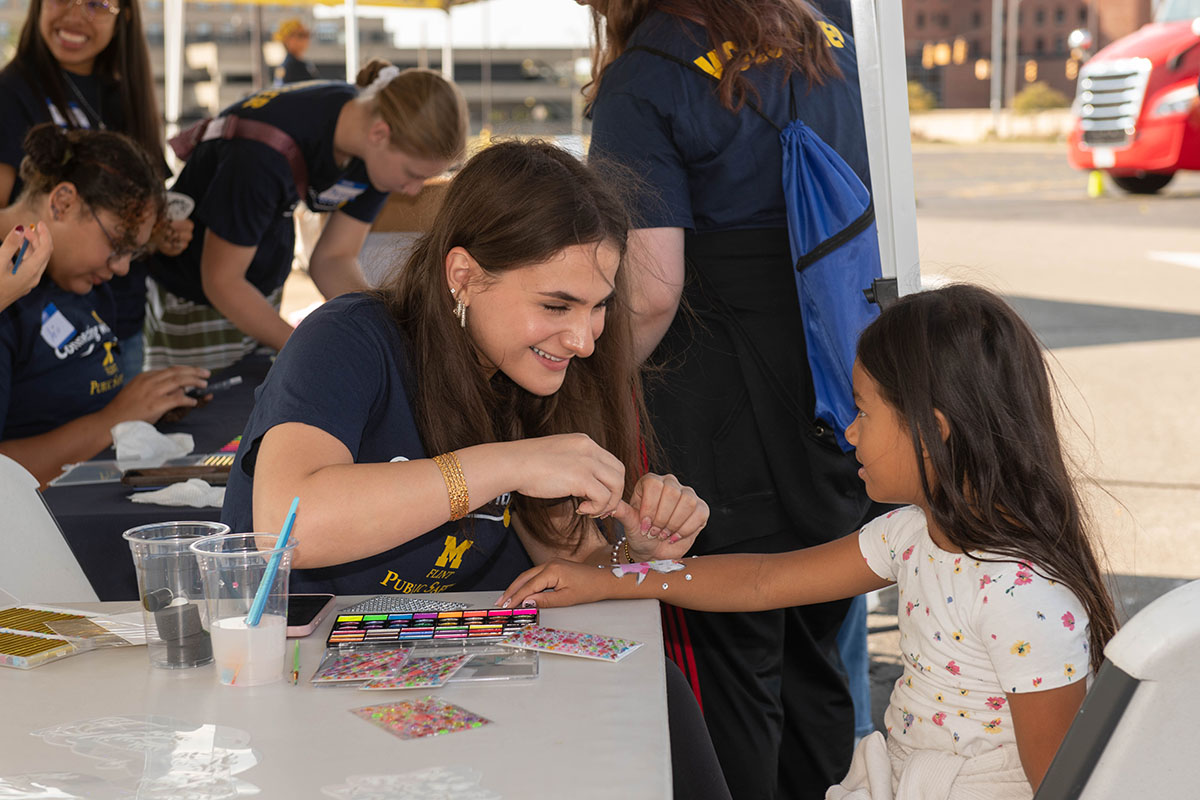 A UM-Flint volunteer giving a child a temporary tattoo
