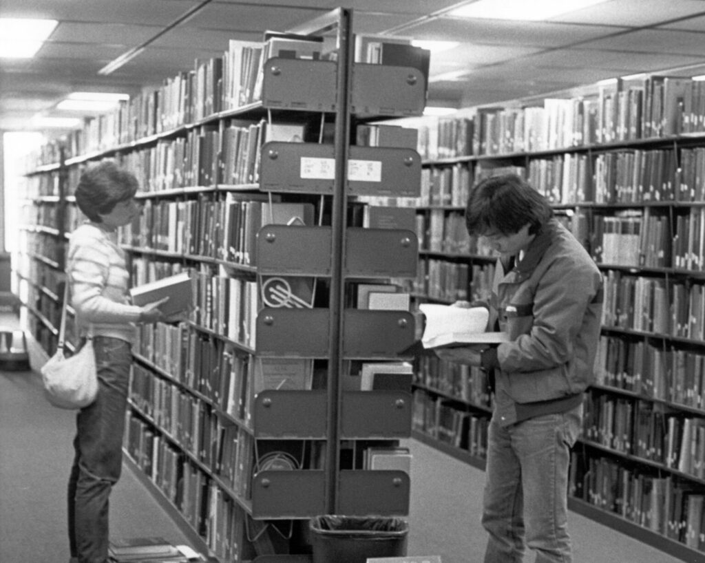 Black and white image of two students looking at books in a library