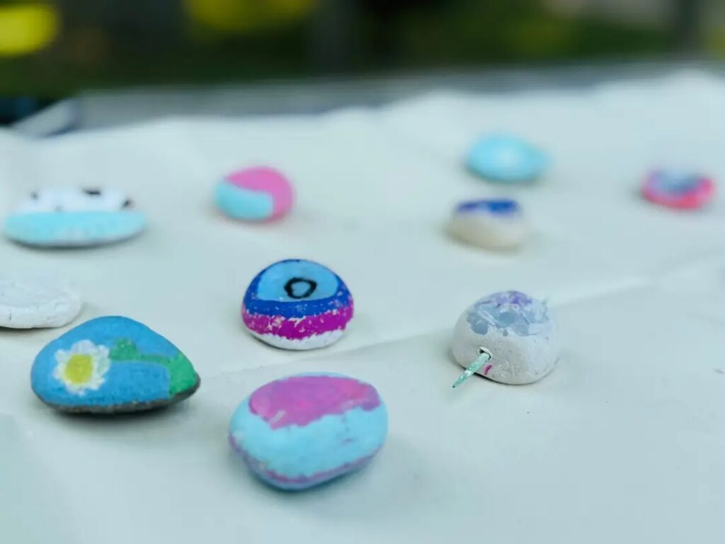 Several multi-colored, painted stones made of clay are laid out on a picnic table