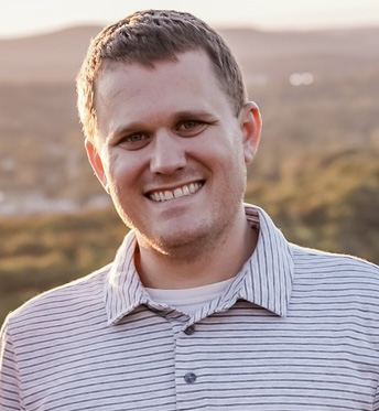 A man wearing a polo shirt smiling in front of a rolling landscape