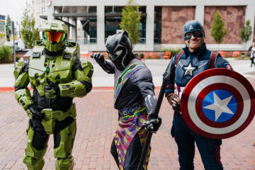 Three individuals dressed in superhero costumes: one in green armor, one as Black Panther, and one as Captain America with a shield.