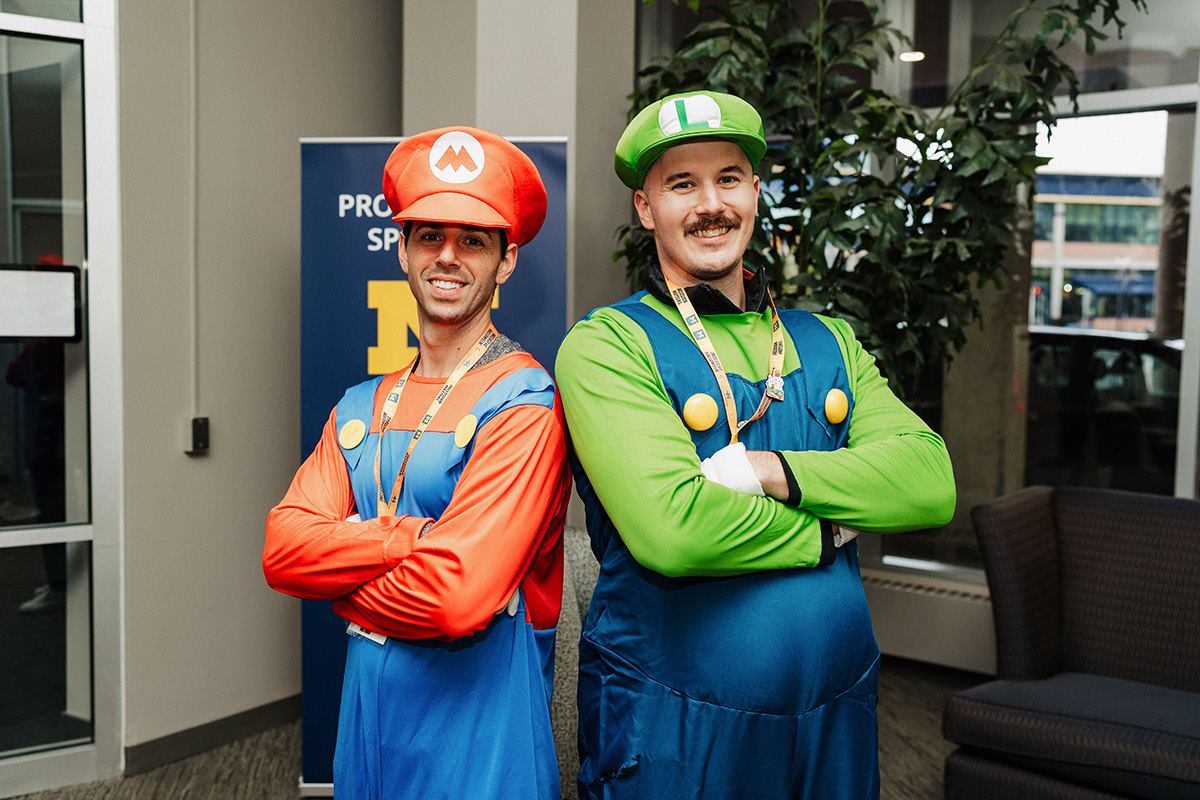 Two individuals dressed as Mario and Luigi, standing with arms crossed in a casual setting.