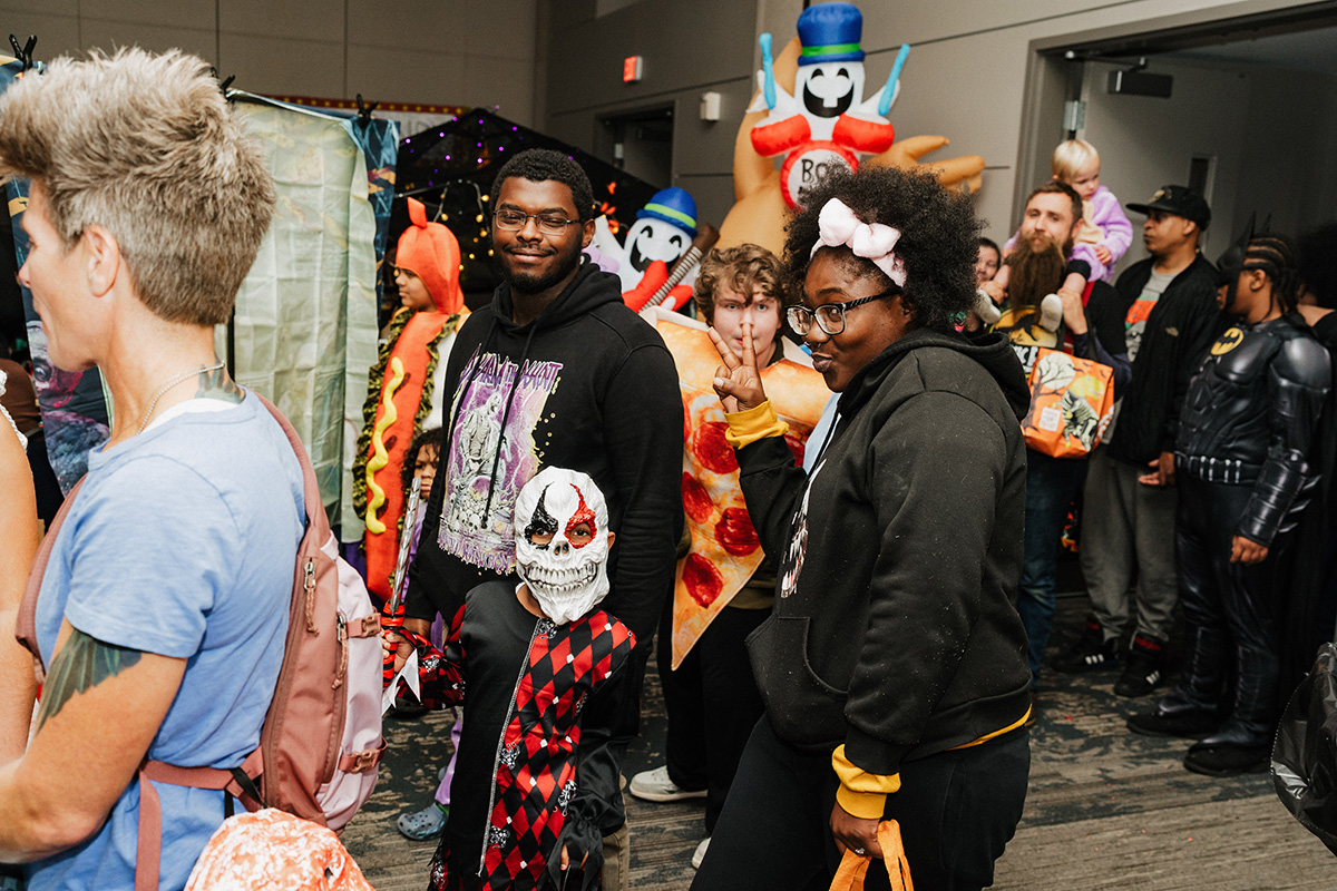 A group of people in costumes, including a child with a skull mask and a person dressed as Batman, at a festive event.