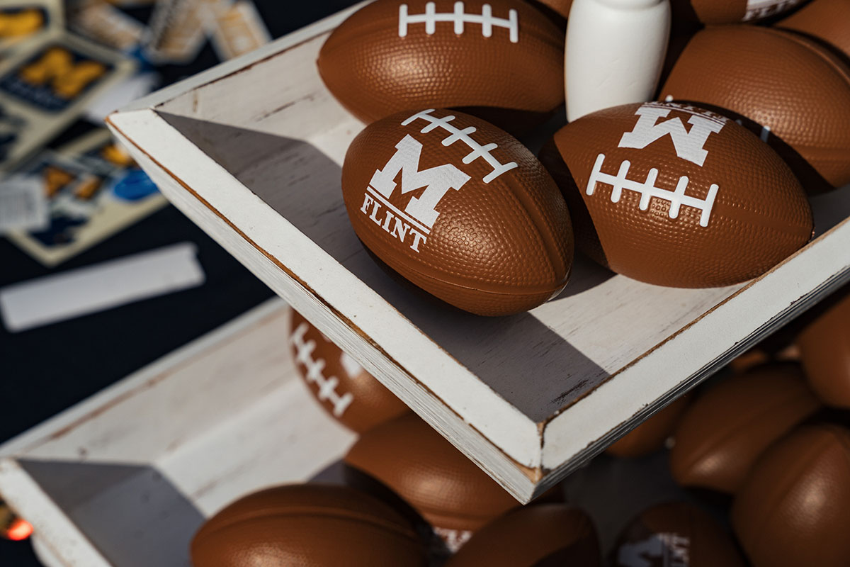 A display of brown footballs with white laces, some labeled with "M FLINT," on a wooden shelf.
