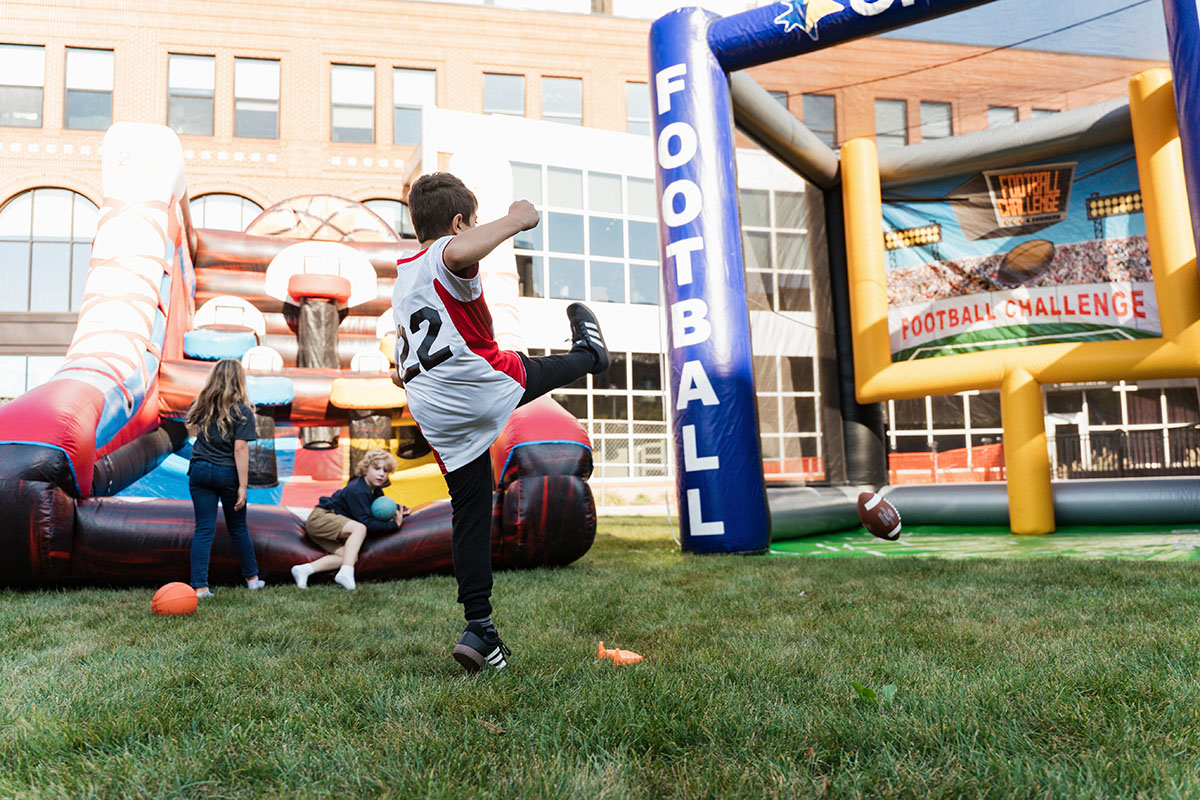 A child in a red and white jersey kicks a football towards a large inflatable football challenge game.