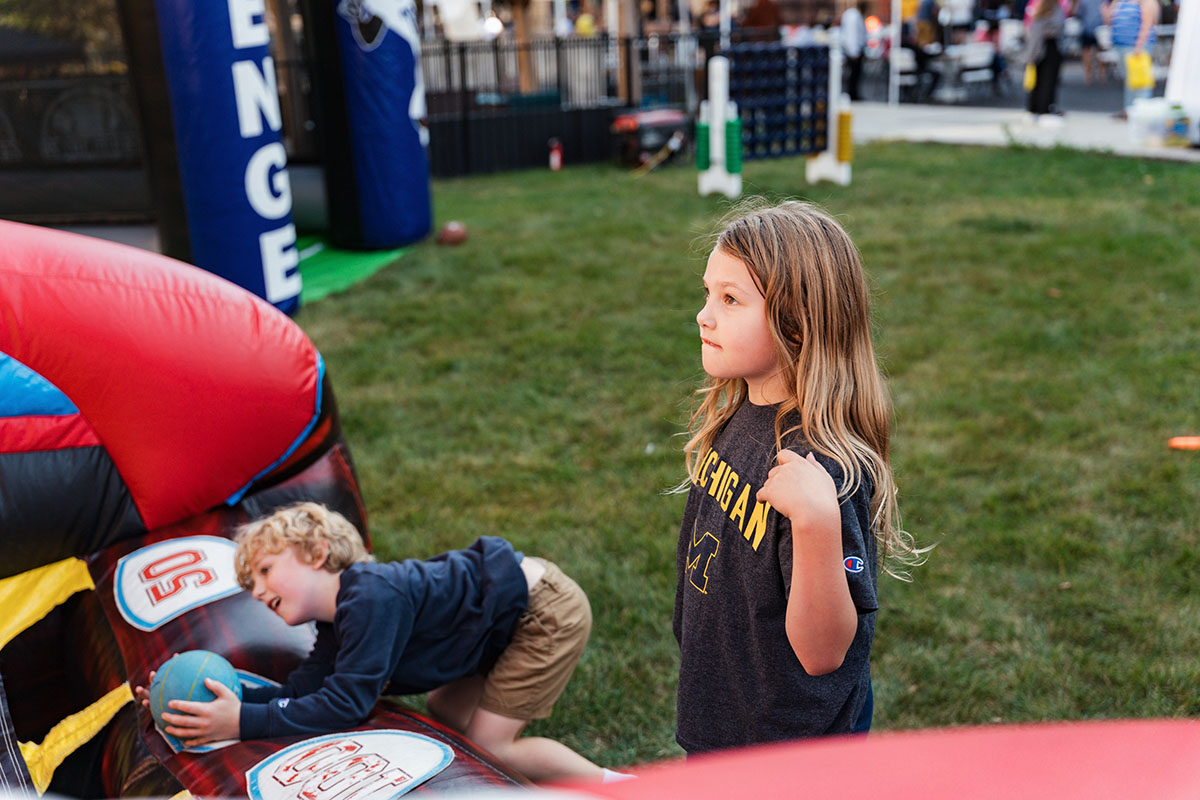 A child in a Michigan t-shirt stands next to a colorful inflatable structure while another child plays nearby.
