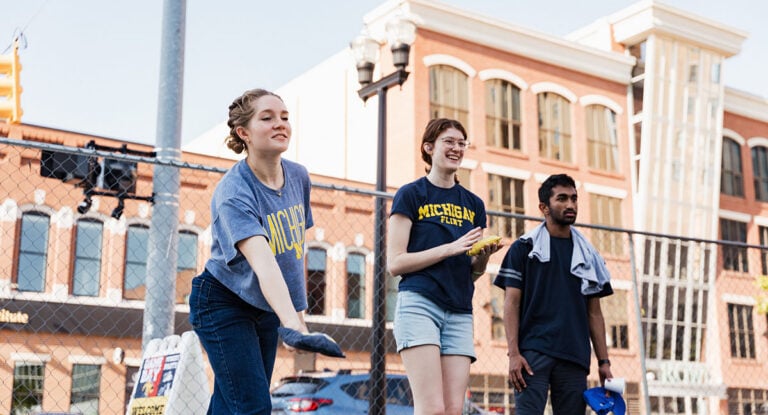 Three people are participating in an outdoor activity, with one person preparing to throw an object while others watch.