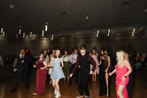 A lively dance floor with people in formal attire enjoying a party, with colorful lights creating a festive atmosphere.