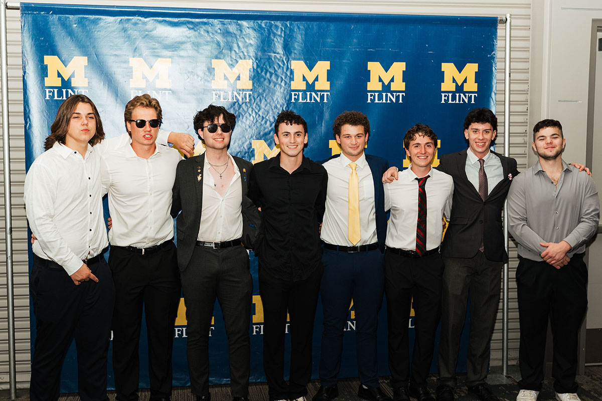 A group of male students posing for a photo in front of a UM-Flint backdrop.