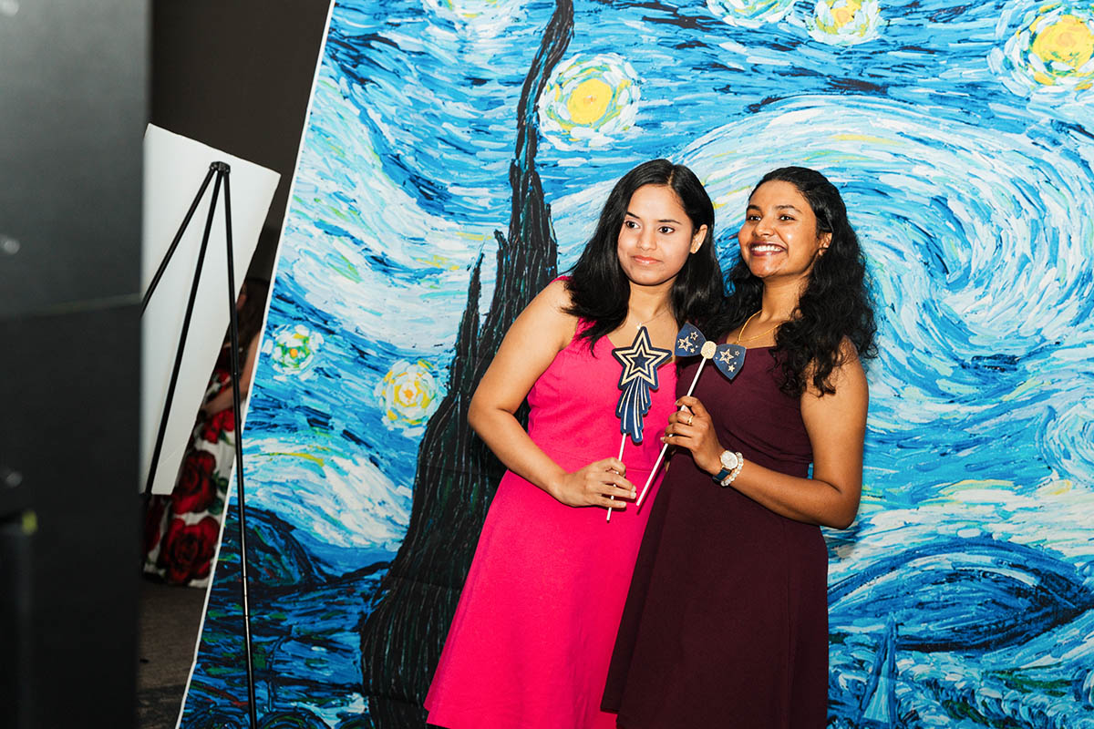 Two female students posing for a photo in front of a starry night backdrop