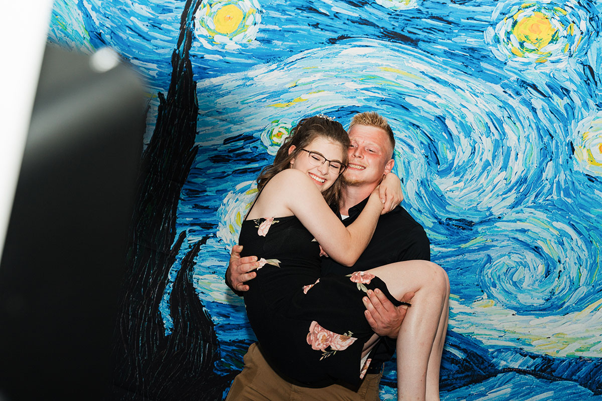 A male student holding up a female student in his arms in front a starry night backdrop