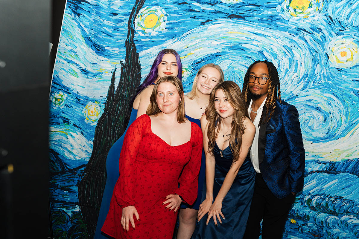 A group of four female students and one male student posing in front of the starry night backdrop.