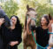 Two women are standing outdoors, each holding a horse. One horse is dark gray and the other is light brown with a white stripe.