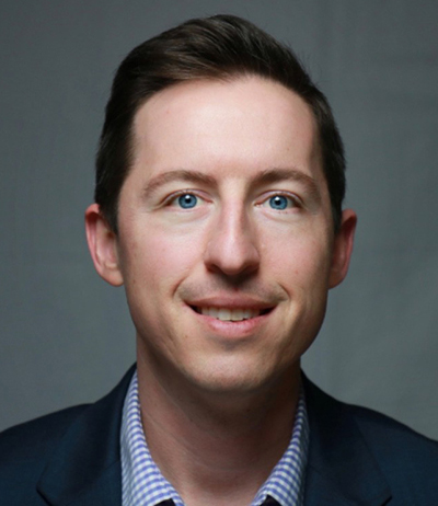 A person wearing a dark blazer and a checkered shirt, with their face blurred for privacy.