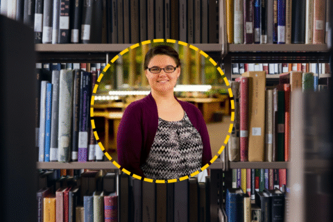 A person stands in a library surrounded by bookshelves filled with various books. The background is softly lit, creating a warm atmosphere.