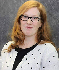 A woman with long, wavy hair wearing a polka dot cardigan and a black top, posing against a gray background.