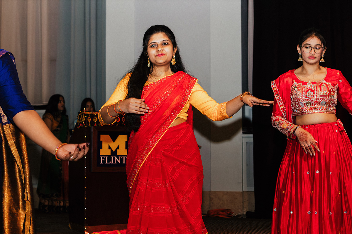 Two women in traditional Indian attire dance at an event, one in a red sari and the other in a red and gold outfit.