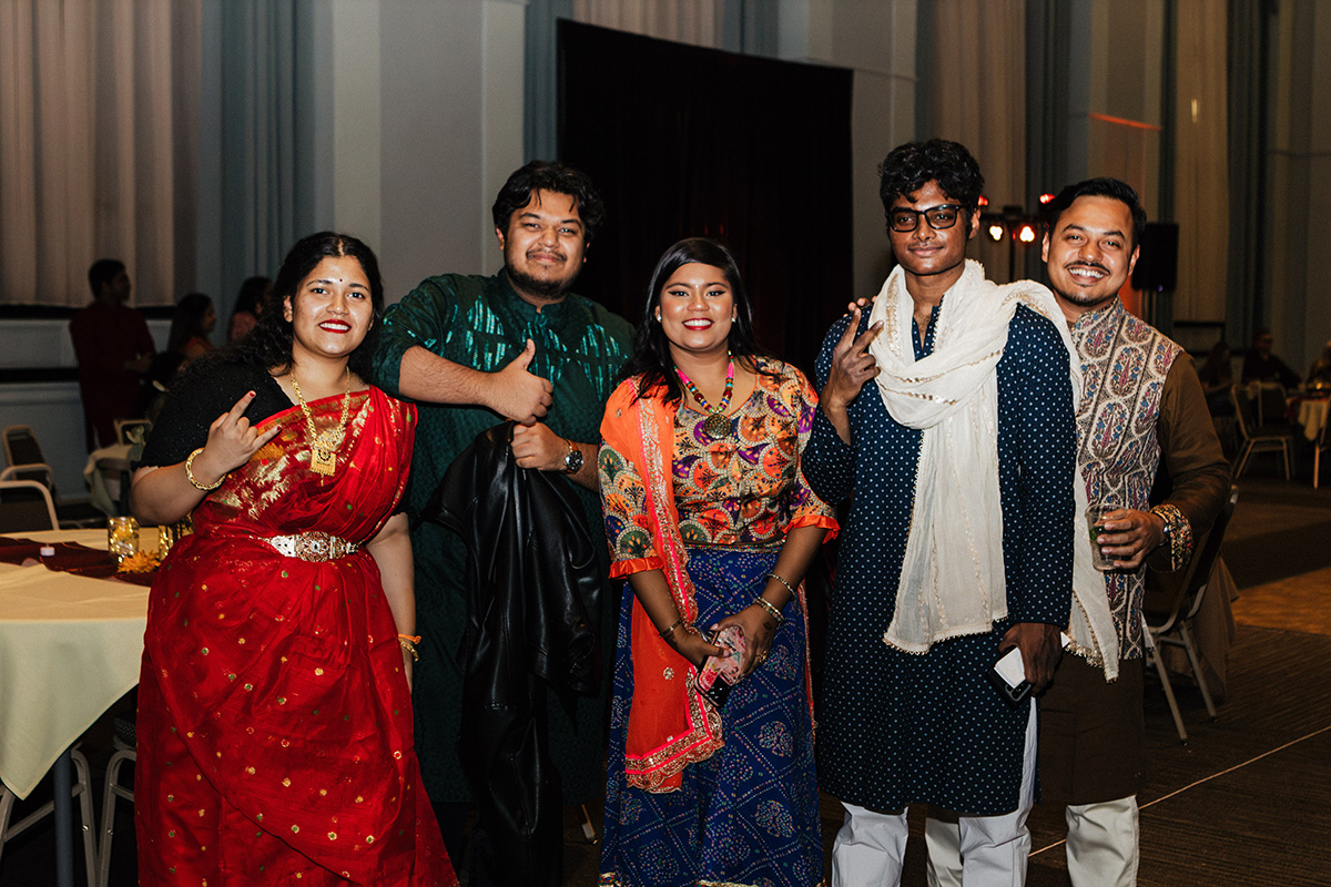 A group of five people dressed in traditional attire, posing together at a festive event.