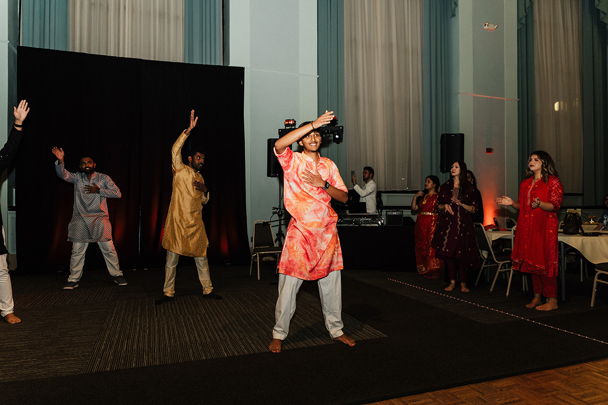 A group of people dancing at an event, wearing traditional attire, with a DJ setup in the background.
