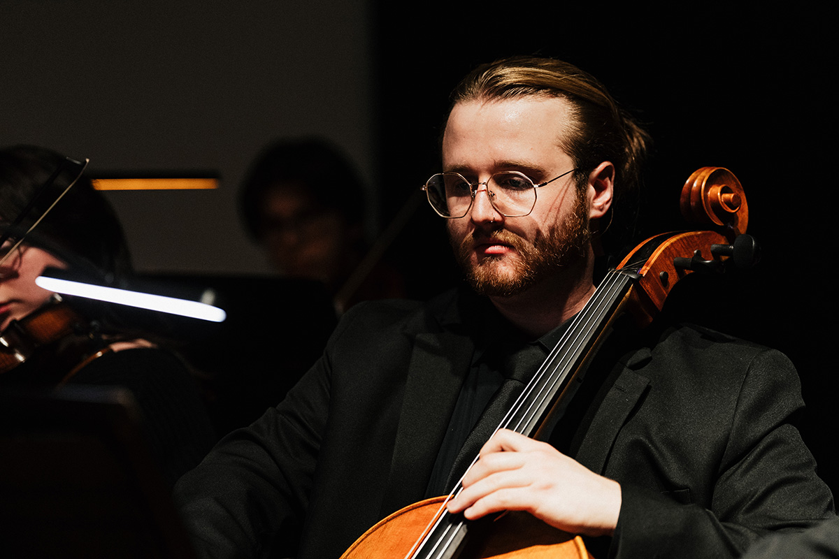 A musician in formal attire playing a cello on stage, with a blurred face for privacy.