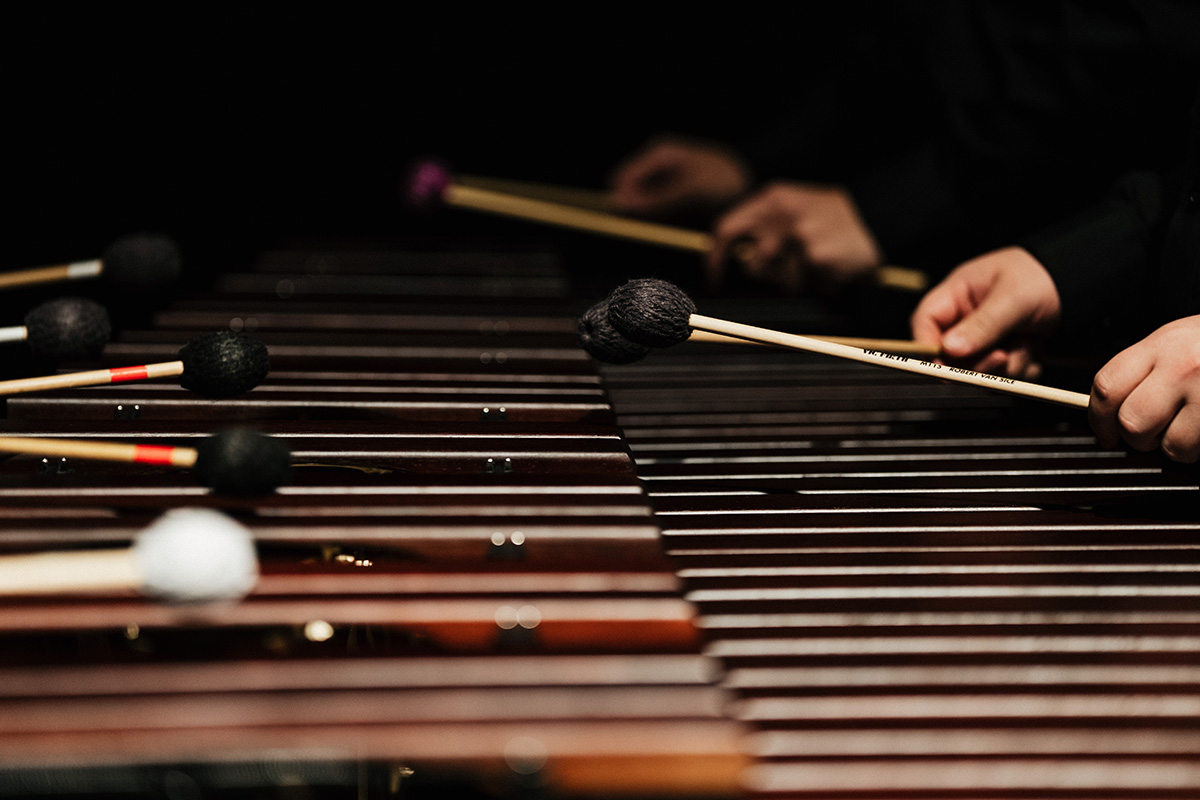 Musicians playing a marimba with mallets, focusing on the wooden bars and their hands.