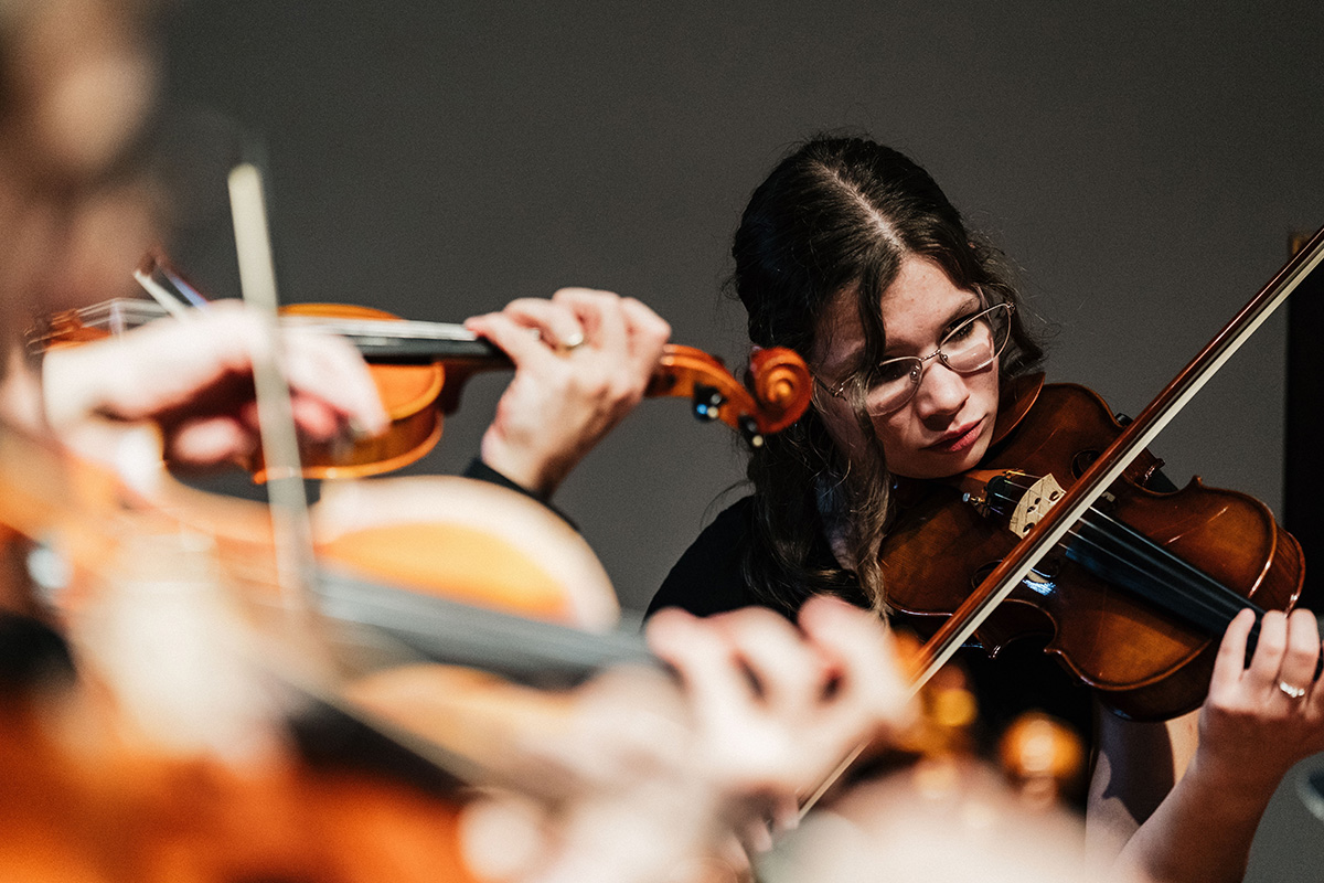 A close-up of musicians playing violins in an ensemble setting.