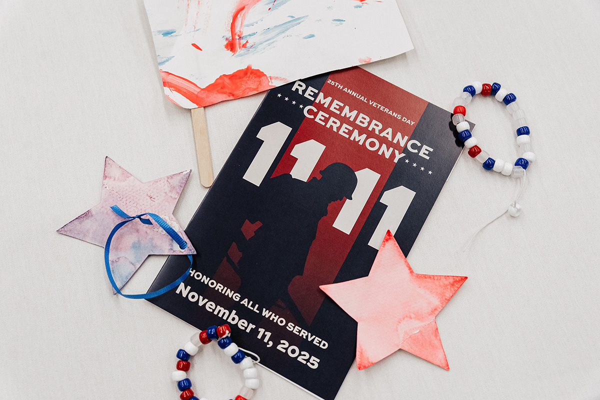 FLINT_Veterans Day 2025_0008 A program for the 25th Annual Veterans Day Remembrance Ceremony on November 11, 2025, surrounded by decorative stars and a beaded bracelet.