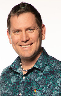 A person wearing a floral patterned shirt and a beaded necklace.